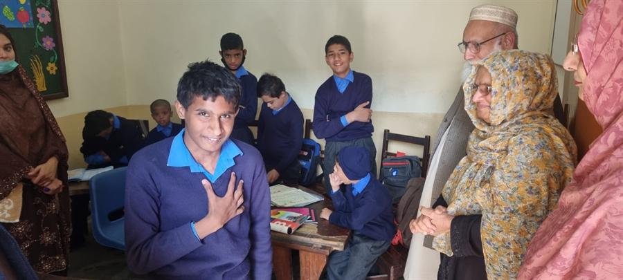 Students at their desks with adults looking on in the classroom