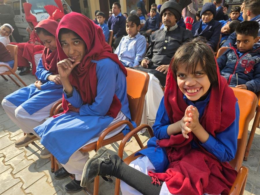 Students seated on orange chairs at an outdoor gathering, two smiling for the camera