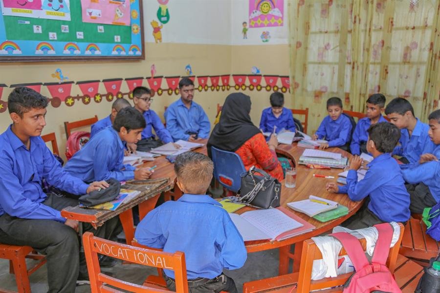 A teacher sitting with students around a large curved desk during a lesson