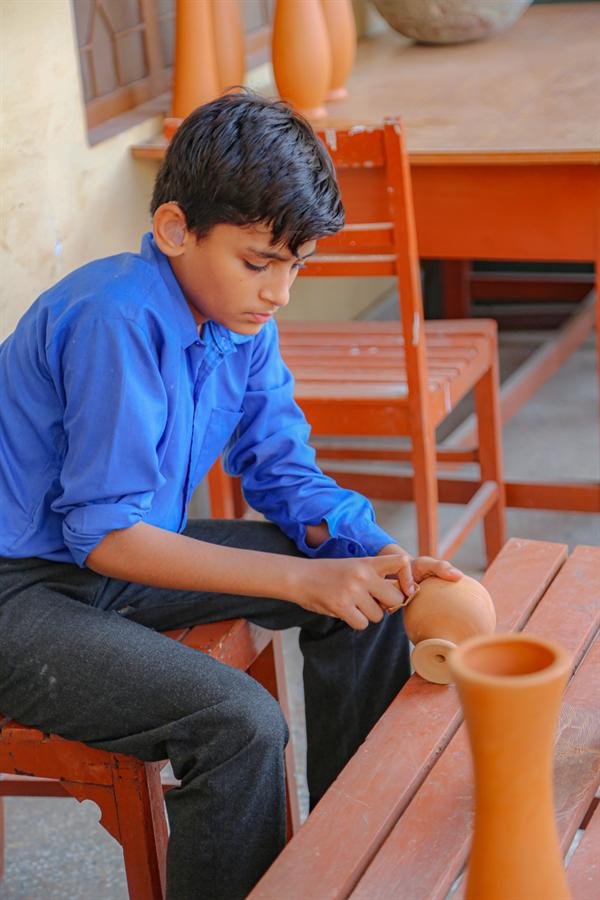 A student working on a clay pot with more pots on the bench beside them