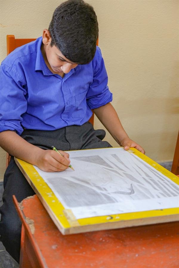 A student drawing on a sketchpad at a desk