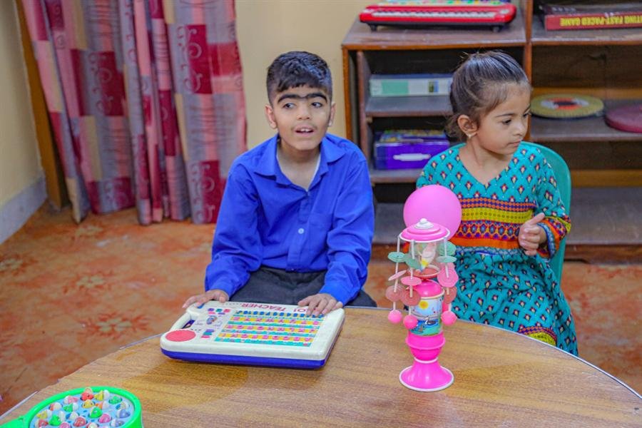 A boy and a girl at a table with a toy keyboard and other learning toys