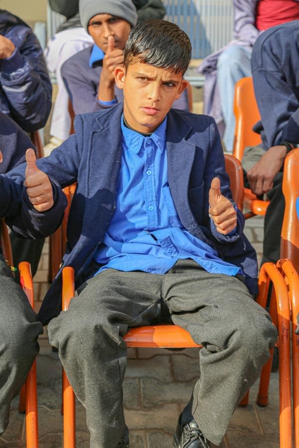 A student in a blazer seated on a chair giving two thumbs-up