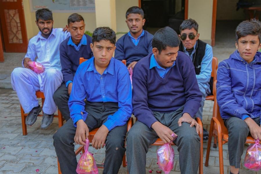 Students sitting in a row on chairs, holding small pink gift bags