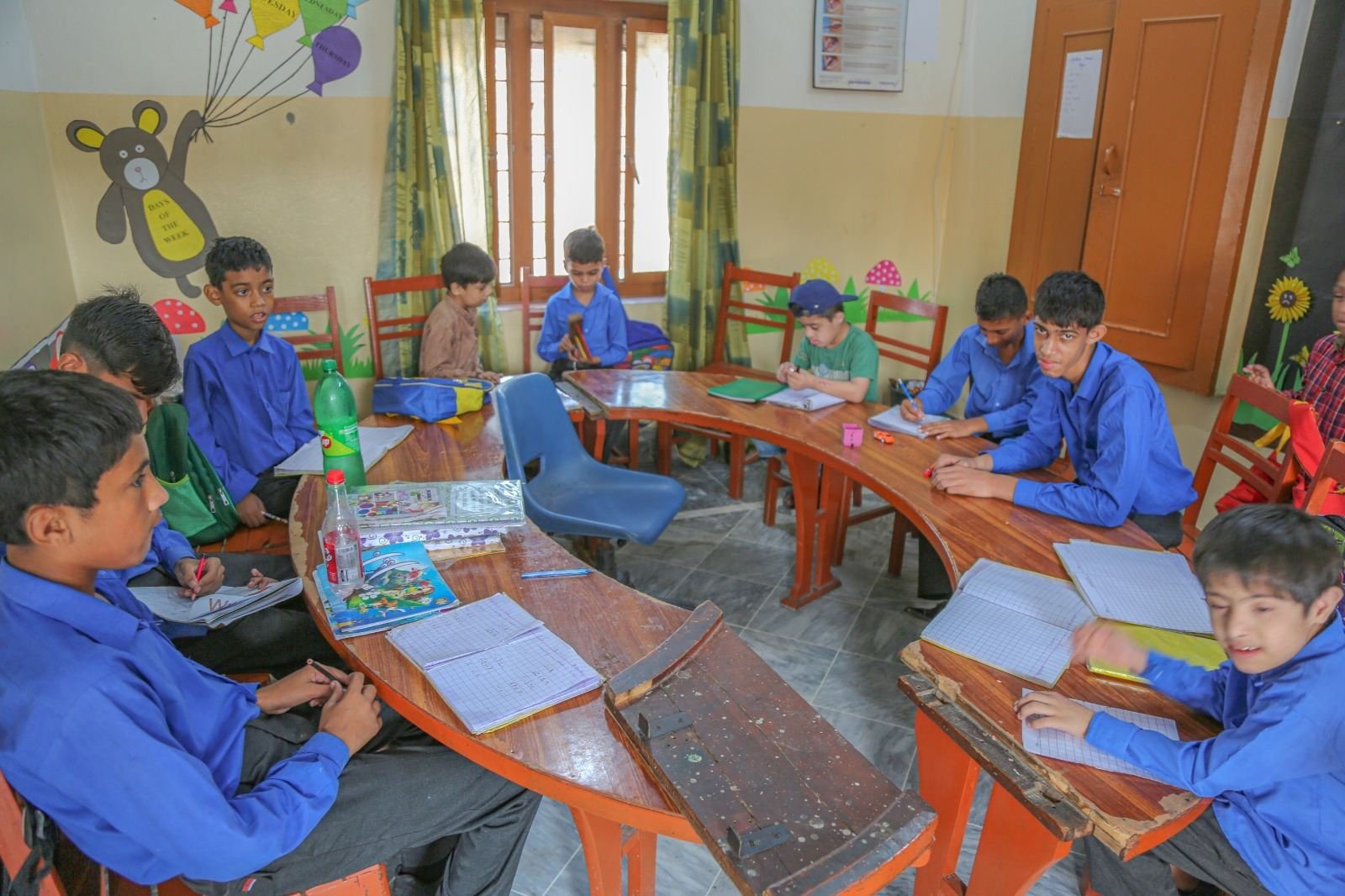 Students of Al Qasim Institute in blue uniforms studying together around curved desks in their classroom